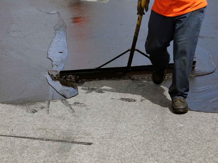 Worker spreading material across an asphalt parking surface