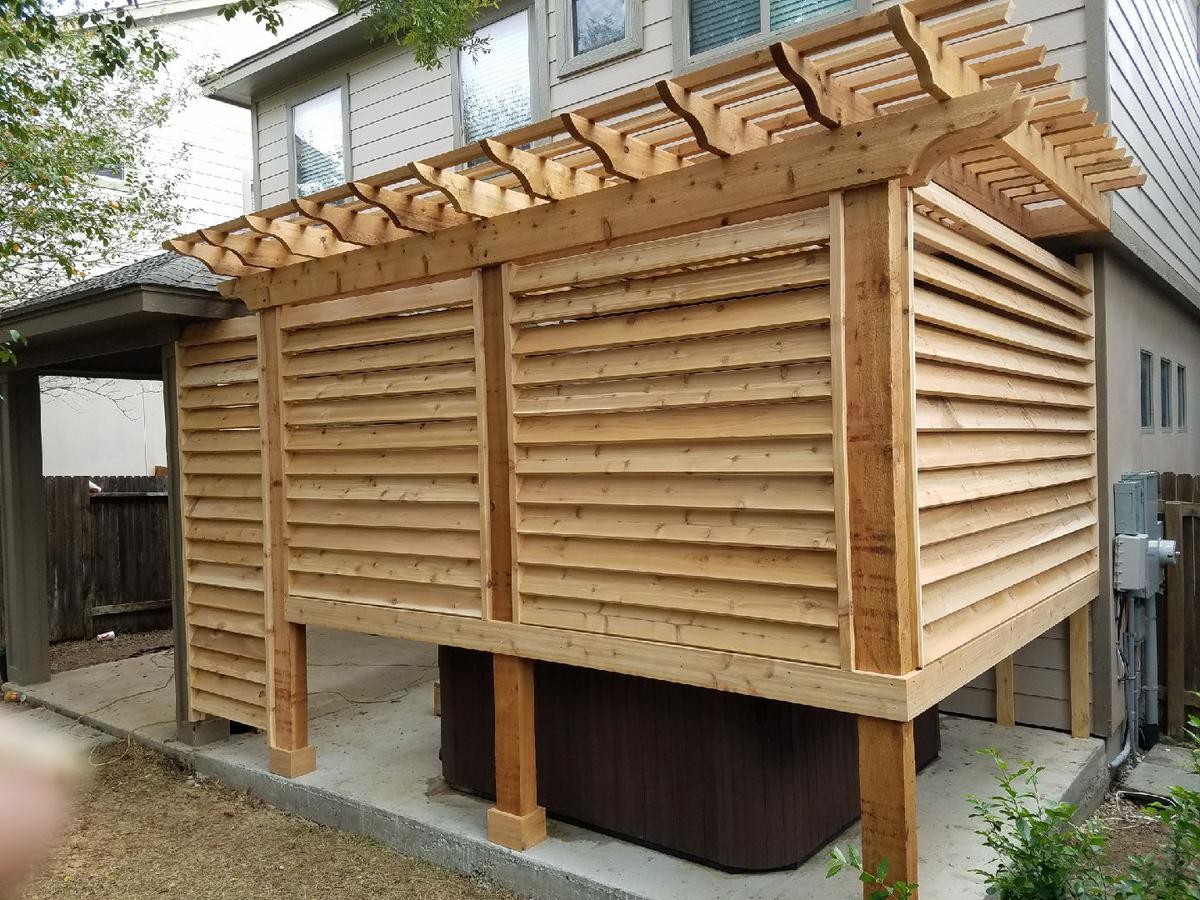 Cedar privacy screen and pergola built around a hot tub on a concrete pad beside a two-story home