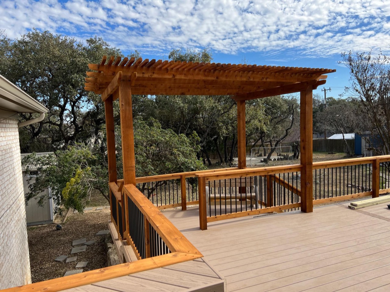 Composite deck with black metal baluster railing and cedar pergola under Hill Country oak trees