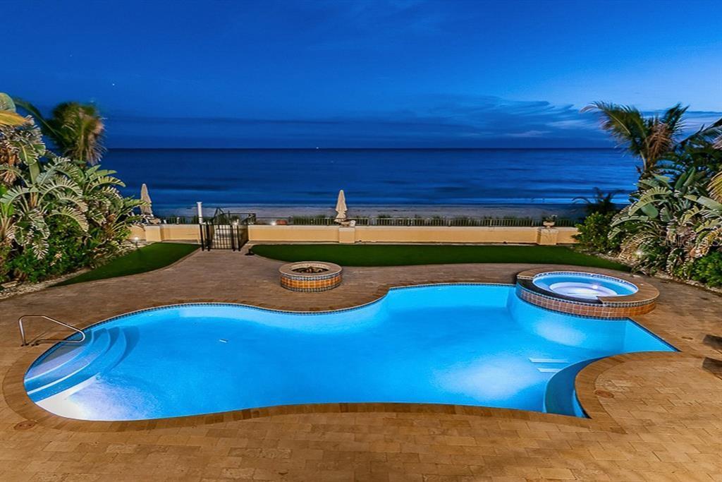 Freeform pool with attached spa and brick paver deck overlooking the Gulf at dusk